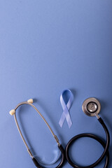 Directly above shot of blue stomach cancer awareness ribbon and stethoscope over blue background