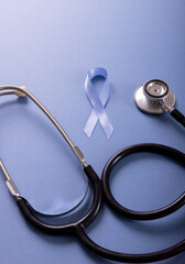 High angle view of blue stomach cancer awareness ribbon with stethoscope on blue background