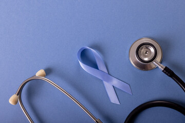 Directly above shot of blue stomach cancer awareness ribbon and stethoscope on blue background