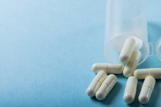 High Angle Close-up Of White Capsules Spilled From Bottle Over Blue Background, Copy Space