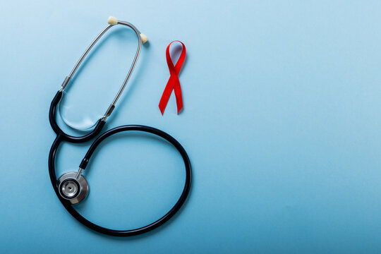 Directly above shot of red aids awareness ribbon with stethoscope over blue background, copy space