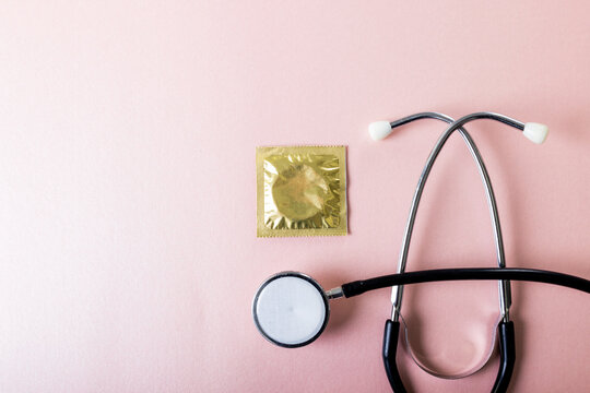 Directly above shot of stethoscope with condom in pack against pink background, copy space