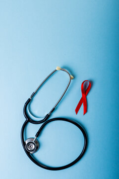 Directly above shot of red aids awareness ribbon and stethoscope against blue background, copy space
