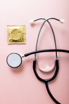 Directly above shot of condom in pack with stethoscope against pink background, copy space