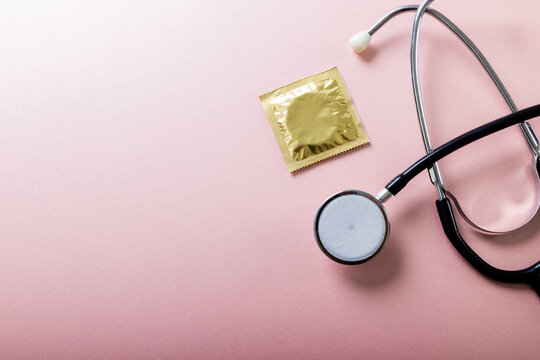 Overhead view of condom in pack with stethoscope against pink background, copy space
