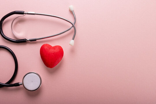 Directly above shot of stethoscope and red heart shape against pink background, copy space