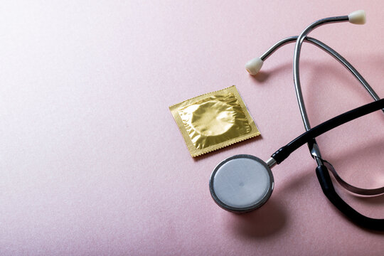 High angle view of condom in pack with stethoscope against pink background, copy space