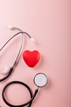 Overhead view of stethoscope with red heart shape against pink background, copy space