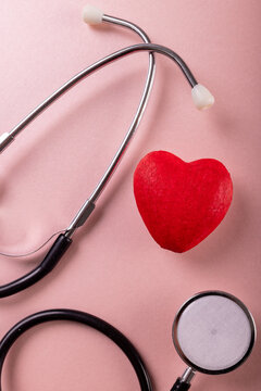 Overhead close-up of stethoscope with red heart shape against pink background, copy space