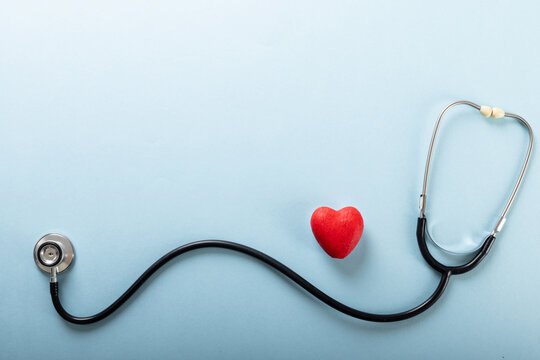 Directly above shot of stethoscope and red heart shape against blue background, copy space
