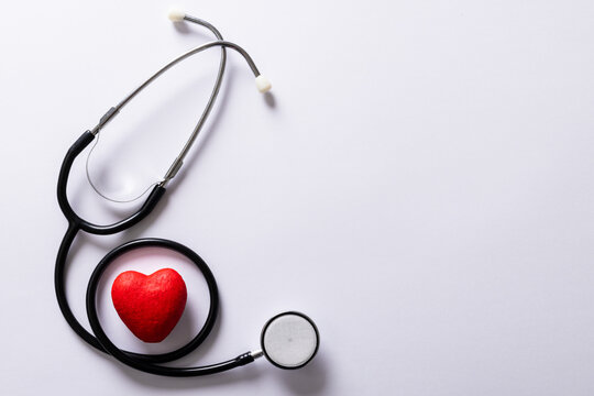 Overhead view of red heart shape with stethoscope against white background, copy space