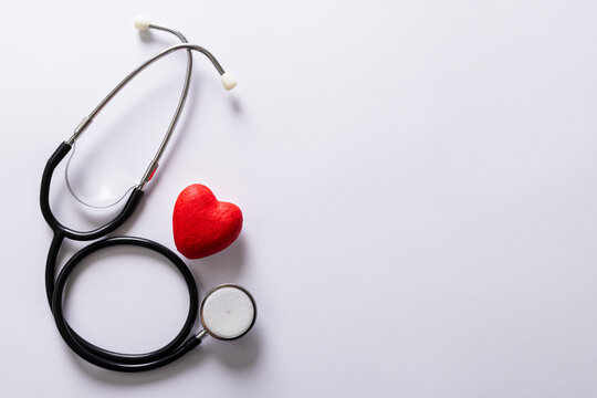 Overhead view of red heart shape and stethoscope against white background, copy space