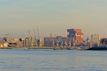 Antwerp skyline from across river Scheldt in wam evening light, featuring the MAS museum with it`s collection of old industrial cranes and new apartment buildings 