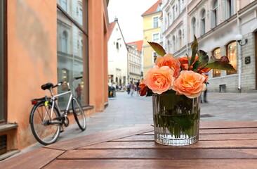 orange roses flowers in glass on wooden table street cafe and bike on pavement in Medieval city Tallinn od town houses travel to Estonia 