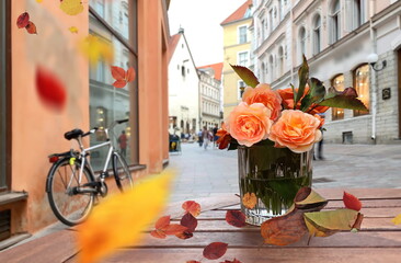 Autumn leaves and  orange roses flowers in glass on wooden table rainy street cafe and bike on pavement in Medieval city Tallinn od town houses travel to Estonia 