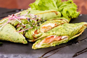 spinach rolls with salmon and microgreens on a black ceramic