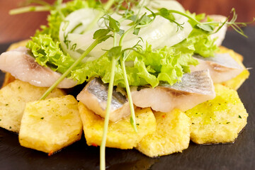 dish with potatoes, herring in a sauce with microgreens and lettuce