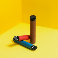 Colorful disposable electronic cigarettes with shadows on a yellow background. The concept of...