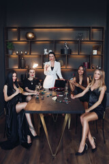 Elegant girls in black playing cards and drinking champagne