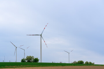Fototapeta na wymiar Wind turbines on a blue background stand on a green field with rare green trees on a spring day, green energy saves nature and beauty