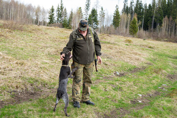 Old Hunter in the woods with his dog. Male hunter hunting with his hunting dog outdoors. German wirehaired pointer. Hunter with  his shotgun in middle of nature.
