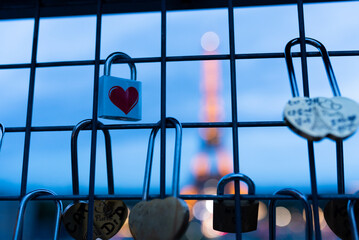 Illuminated Eiffel Tower is seen at night behind fence filled with locks and lockers with heart...