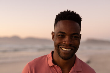 Close-up portrait of smiling african american young man at beach against clear sky during sunset