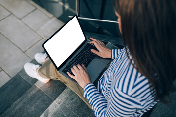 Naklejka premium Young woman freelancer working online using her laptop, sitting on stairs.