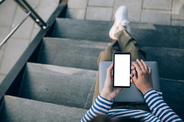 Young woman freelancer working online using her laptop, sitting on stairs.