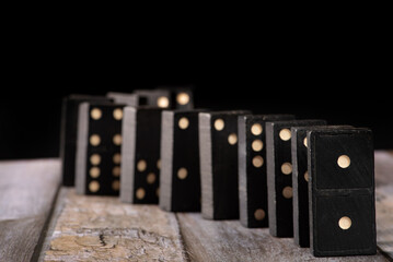 Dominoes, old domino pieces lined up on wooden surface, dark background, selective focus on first piece.