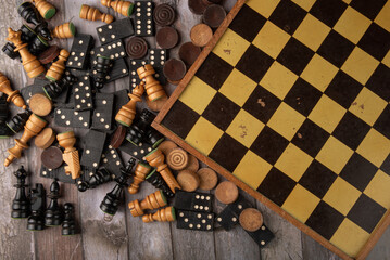 Antique dominoes, chess and checkers played randomly on a board on a rustic wooden surface, dark...