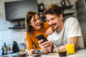 Two people young couple adult man and woman husband and wife or boyfriend with girlfriend in the kitchen in the morning with coffee juice mobile phone and digital tablet talking and chat happy smile