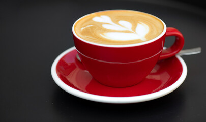 Red cup of latte with art on black table. Top view. Place for text.