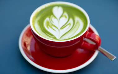 Cup of matcha latte in red cup on blue background in a cafe with copy space. High quality photo.