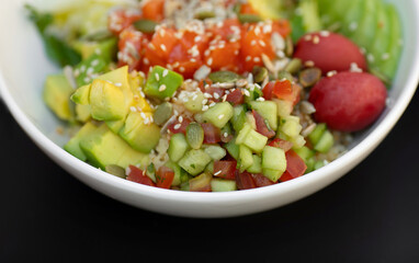 Salmon fresh vegetable salad of tomato, avocado, cucumber, lettuce and spinach. Healthy and detox food concept. Ketogenic diet. Buddha bowl dish on black background, top view.