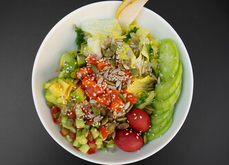 Poke bowl with salmon, rice, avocado, edamame beans, cucumber and radish in white bowl.