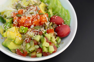 Poke bowl with salmon, rice, avocado, edamame beans, cucumber and radish in white bowl.