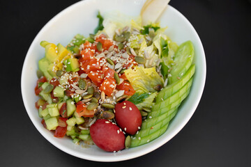 Poke bowl with salmon, rice, avocado, edamame beans, cucumber and radish in white bowl.
