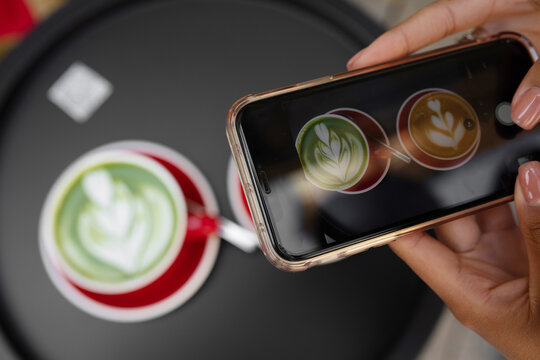 Young girl using Photography of smartphone of latte art coffee on mobile camera display while shooting.