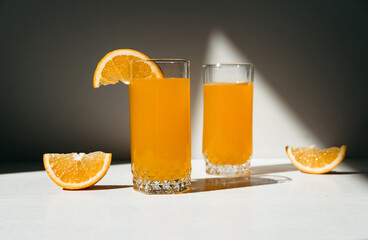 Fresh juice with ripe oranges in two glasses on a white wooden table. Oranges cut into slices. Vitamin juice, a healthy lifestyle. Vegetarianism, vegan, diet, fruit, nectar. Homemade juice, drink.