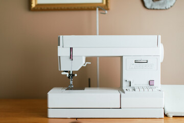 White simple sewing machine set up at a home office desk.