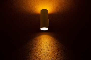 Um holofote iluminando uma parede amarela de concreto texturizado.