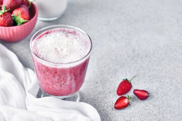 Strawberry coconut milkshake, frappé or smoothie in drinking glass on gray background top view....