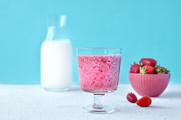 Strawberry coconut milkshake, frappé or smoothie in drinking glass on light blue background. Healthy vegan diet refreshing drink. Healthy food and drink concept.