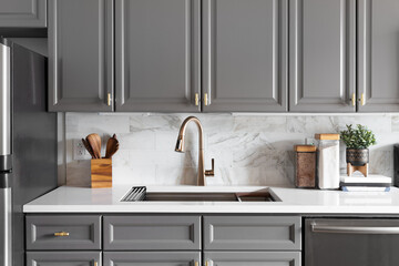 A kitchen sink detail shot with grey cabinets, a white marble countertop and backsplash, and decorations. - obrazy, fototapety, plakaty