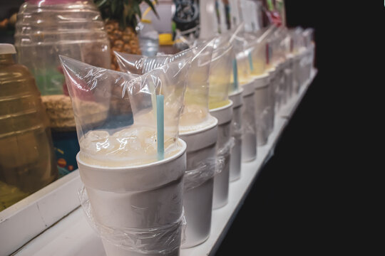 Puesto de aguas y licuados del mercado. Hilera de vasos con aguas de diferentes sabores. Vasos de unicel sellados con papel film y bolsas de pl&aacute;stico.