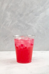 Red refreshing iced cocktail in disposable plastic cup. Summer fruit and berry drink. Take away,...