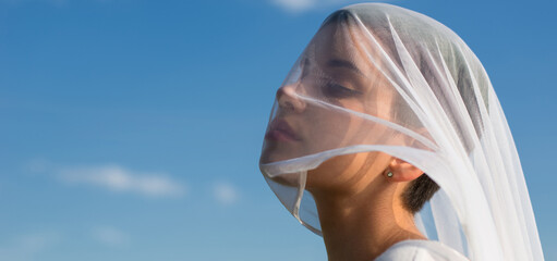 Portrait of beautiful young woman in nature face covered with white silk veil against sky and clouds
