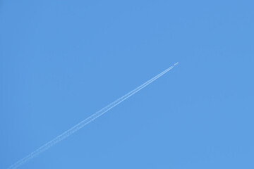 Distant passenger jet plane flying on high altitude on clear blue sky leaving white smoke trace of contrail behind. Air transportation concept