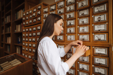 Attractive woman in a white blouse searches for information in the archives of the public library, opens a drawer.